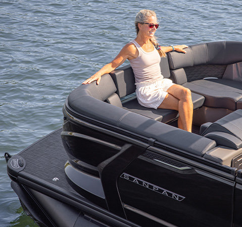 A woman seated in the wraparound bow seating of a black Godfrey Sanpan pontoon boat with premium upholstery.