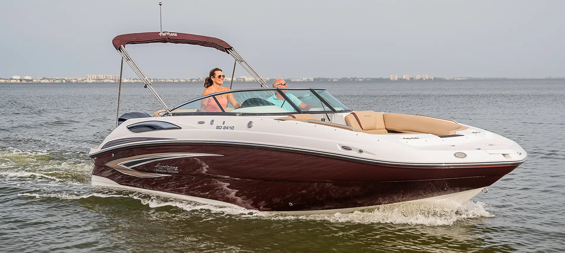 woman driving a black cherry hurricane sundeck 2410 OB deck boat on a lake