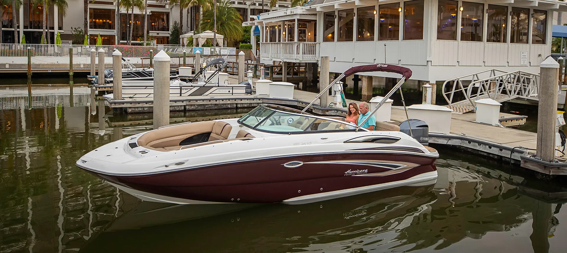 couple sitting on a docked black cherry hurricane sundeck 2410 OB deck boat with hyper platinum graphics
