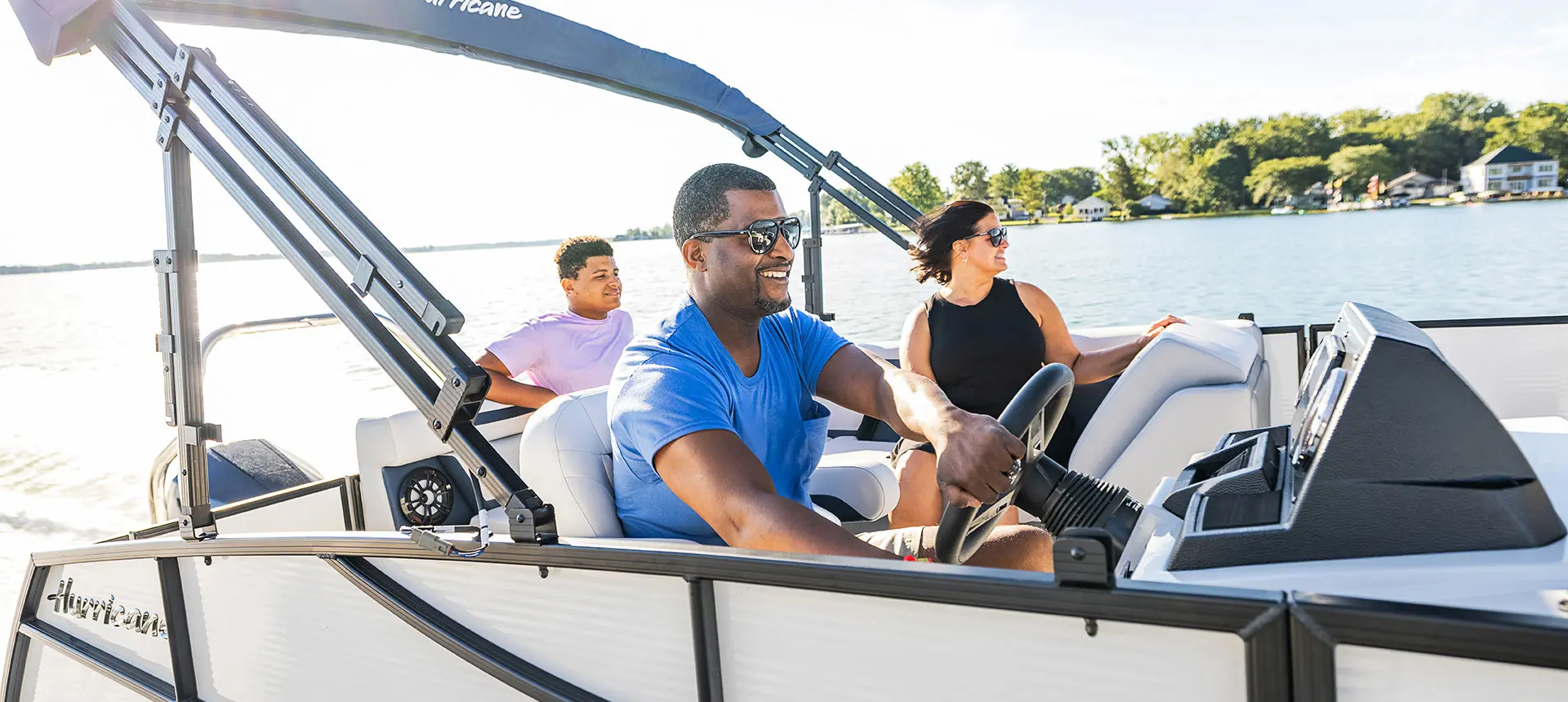 man smiling at the helm of a hurricane fundeck boat while his family sits nearby