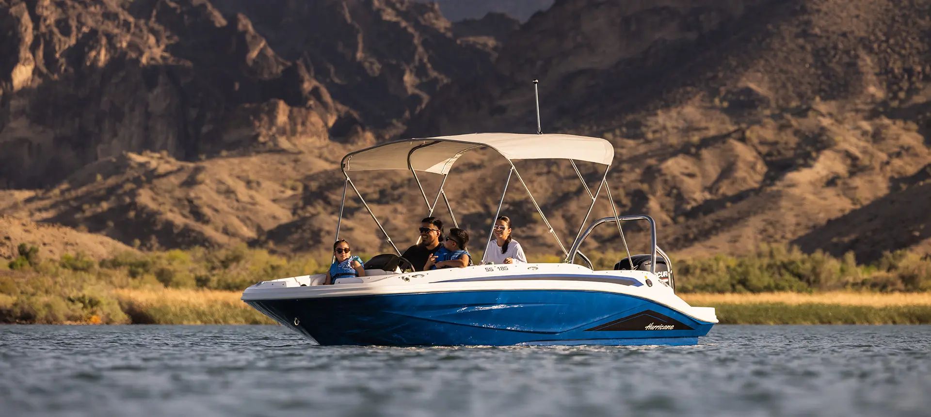 Side profile of a Hurricane SunDeck Sport 185 OB floating on a lake.