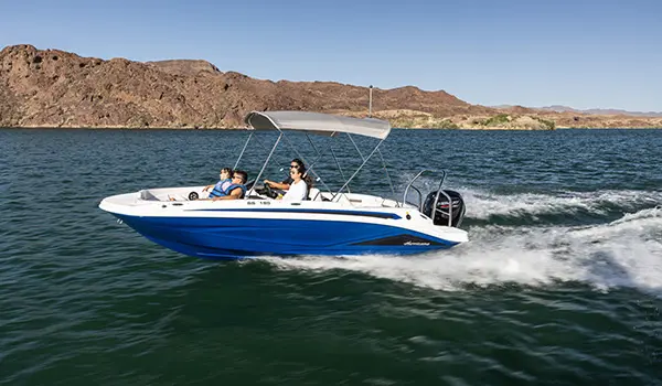 Side profile of a Hurricane SunDeck Sport 185 OB deck boat speeding across a lake.