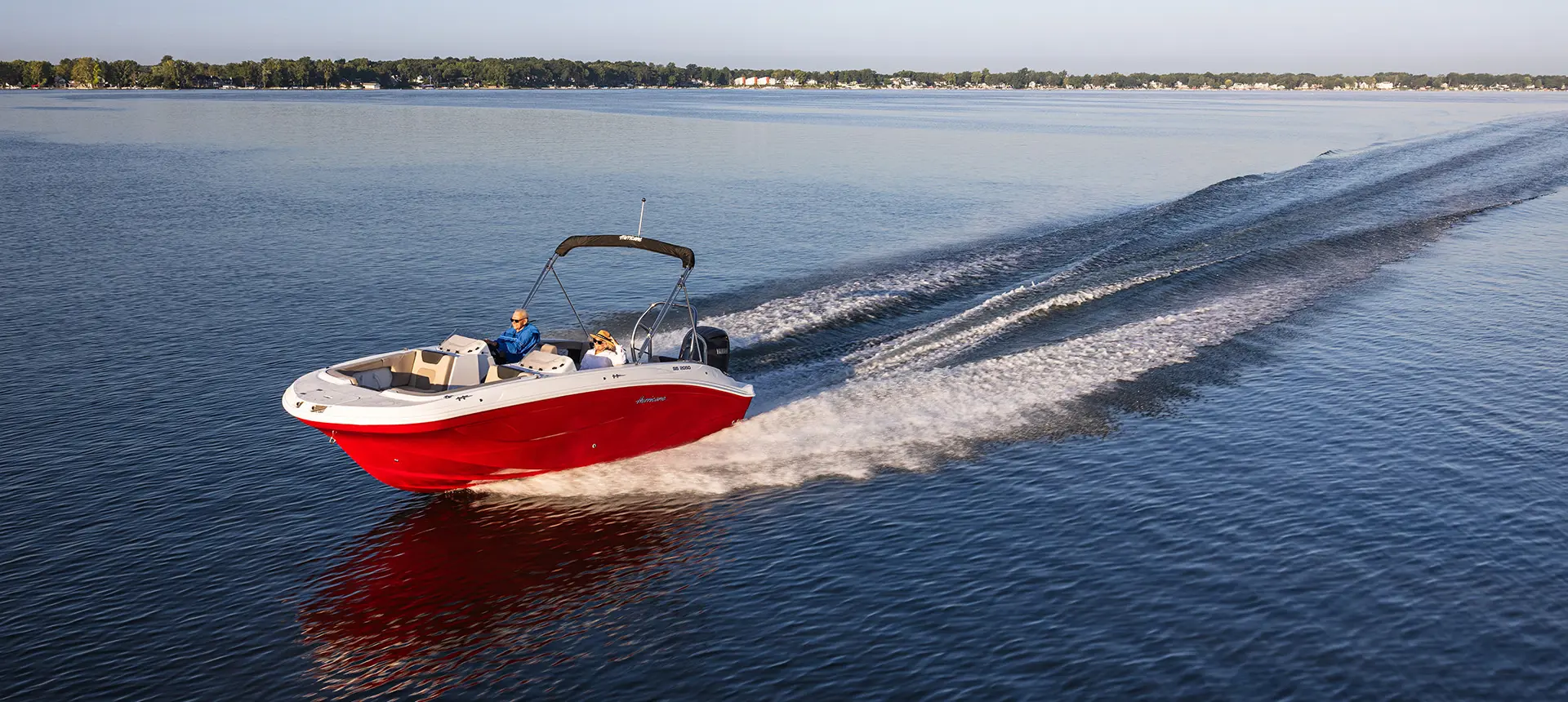 Aerial view of a Hurricane SunDeck Sport 2050 OB deck boat cruising across a lake.
