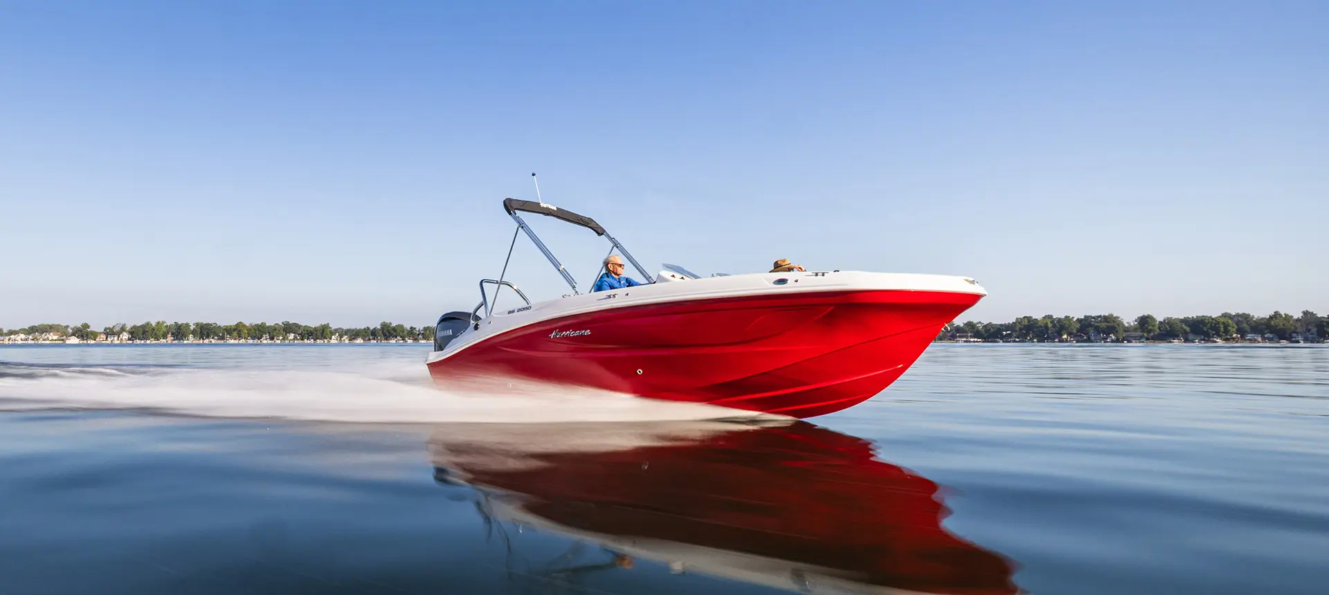 Side view of a Hurricane SunDeck Sport 2050 OB deck boat cruising on a lake.