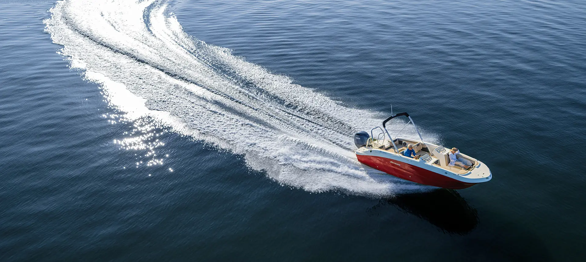 Aerial view of a Hurricane SunDeck Sport 2050 OB deck boat making waves on a lake.