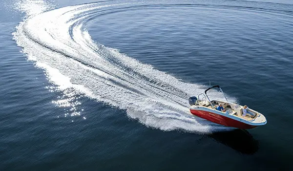 Aerial view of a Hurricane SunDeck Sport 2050 OB deck boat making waves on a lake.
