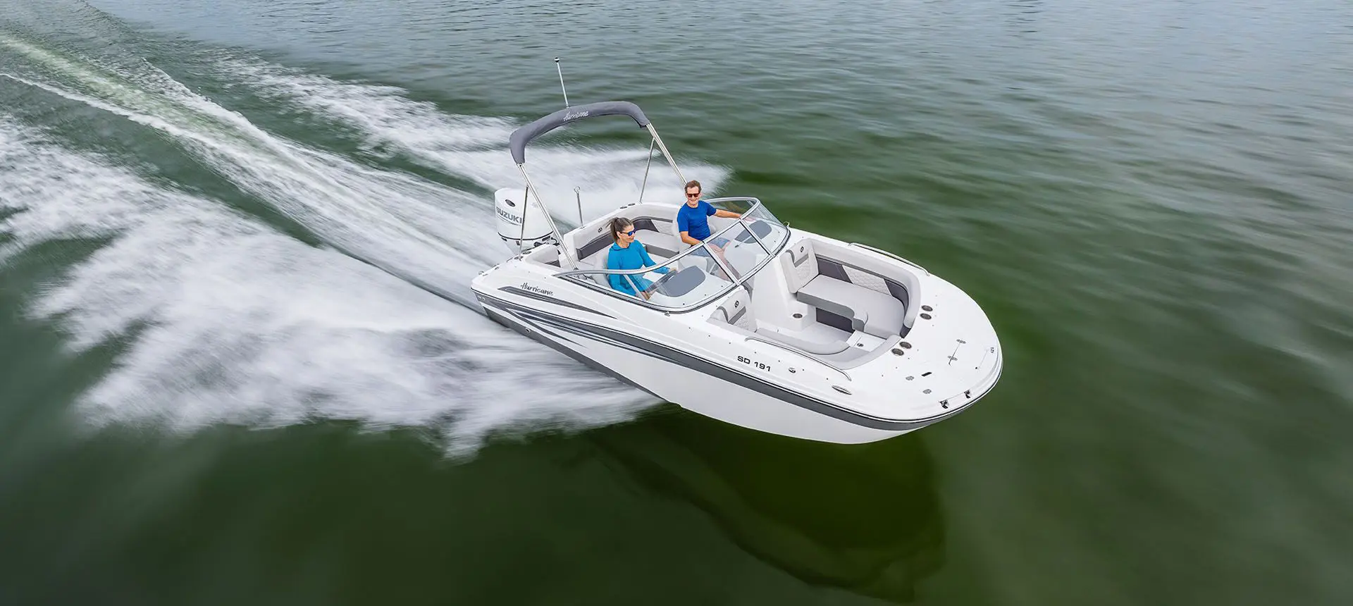 woman at the helm of a hurricane sundeck ob boat speeding across a lake