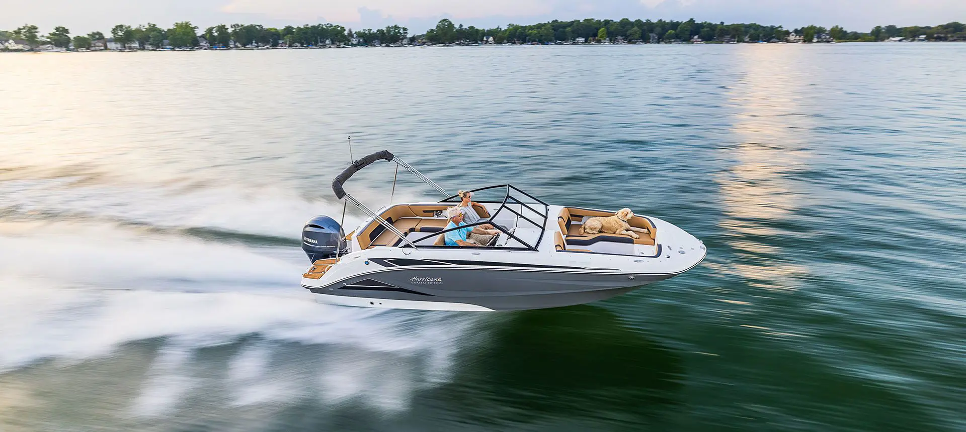 dog on the bow of a hurricane sundeck ob boat while it speeds across a lake