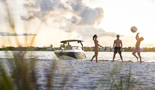 Passengesr playing on the shore with a beach ball near a Hurricane Sundeck 2600 OB deck boat.