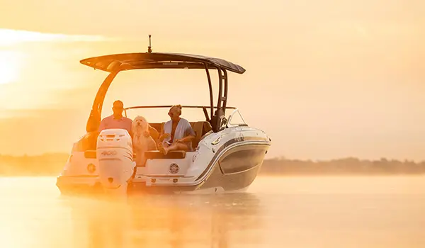 a couple sitting with their dog in the stern seats on a hurricane sundeck 2600 ob deck boat at sunrise