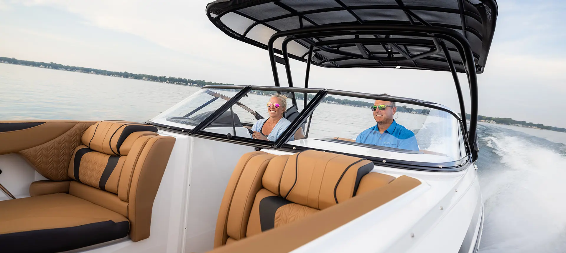 couple smiling while seated in the co-captain's chairs behind the windshield on a hurricane sundeck 2600 ob deck boat