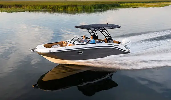 side view of a Hurricane SunDeck 2600 OB deck boat with the canopy up cruising across a lake