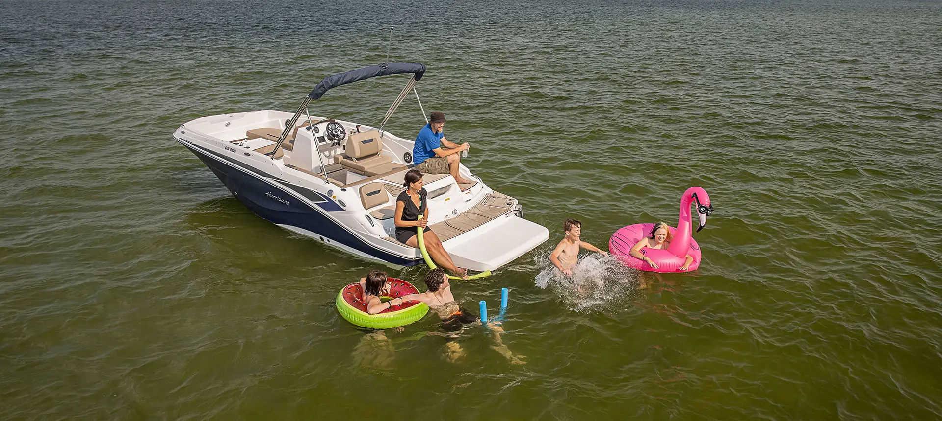 kids swimming around a hurricane sundeck sport i/o boat on a lake