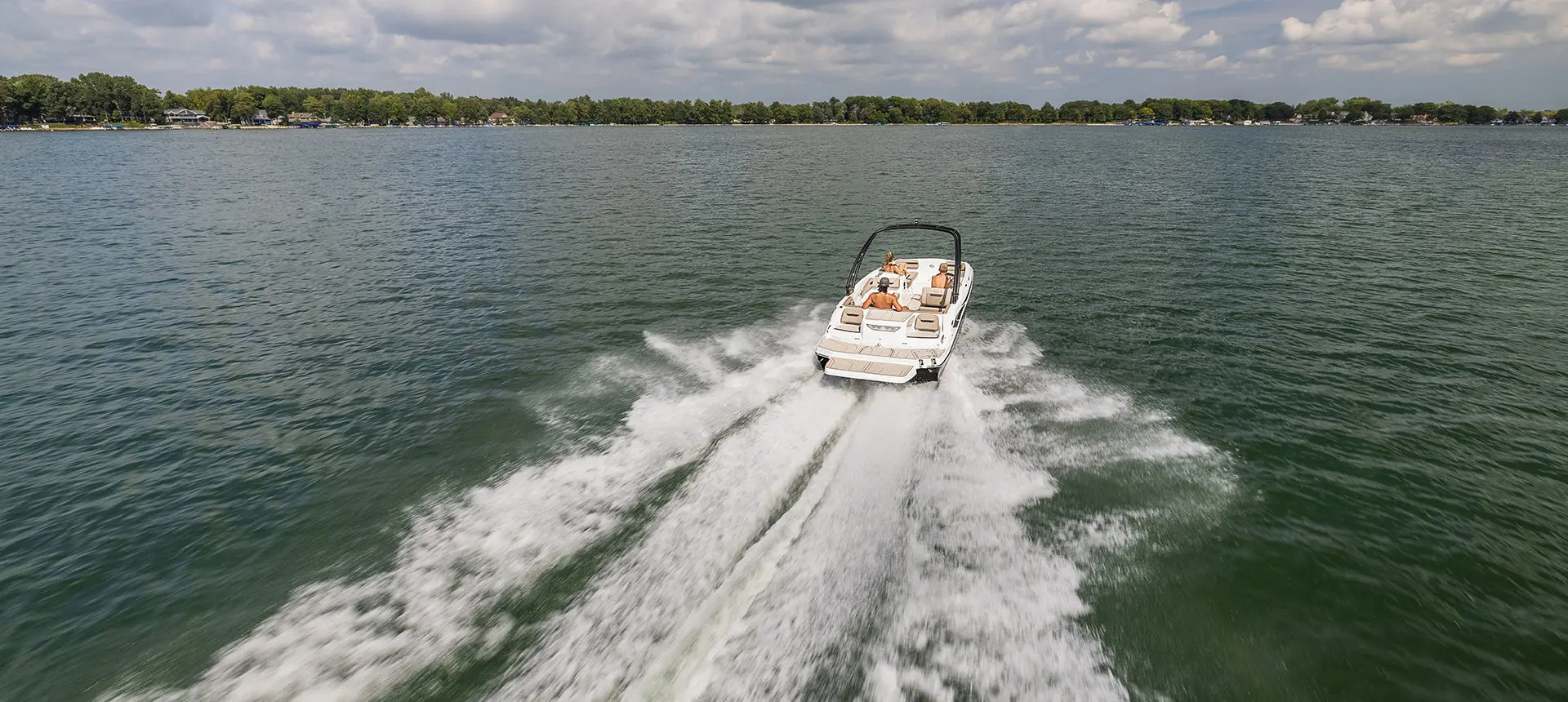 Rear view of a Hurricane SunDeck Sport I/O deck boat cruising across a lake.