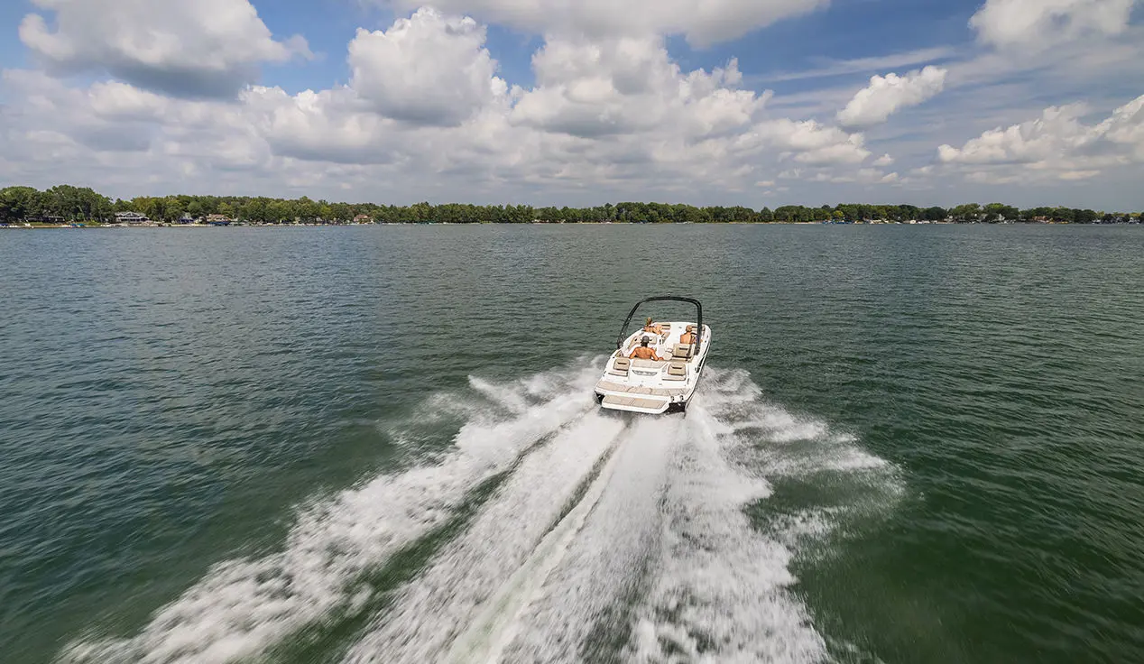 Rear view of a Hurricane SunDeck Sport I/O deck boat cruising across a lake.