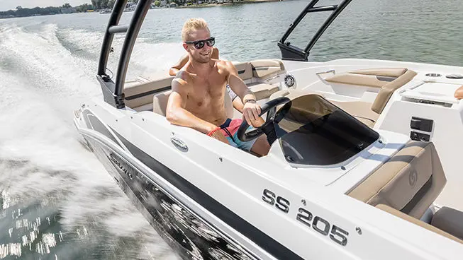 Man smiling at the captain's helm while driving a Hurricane SunDeck Sport I/O deck boat.
