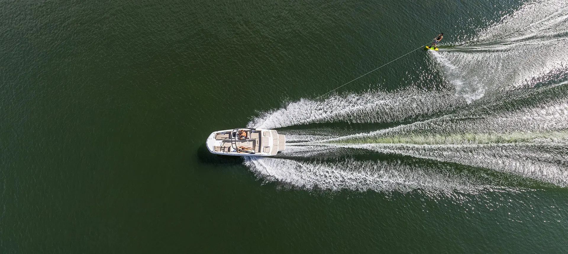 Aerial view of a Hurricane SunDeck Sport I/O deck boat pulling a wake boarder on a lake.
