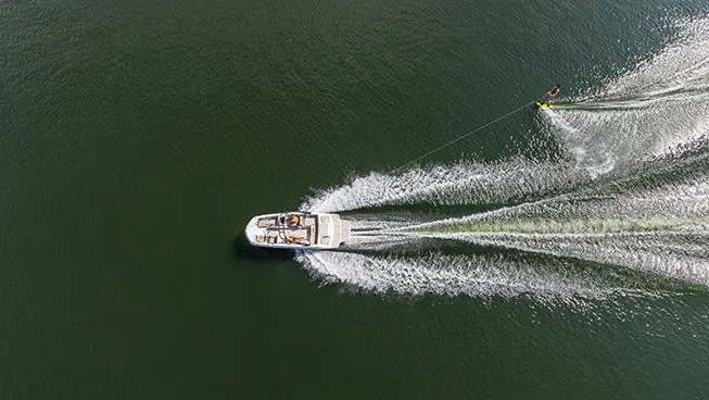 Aerial view of a Hurricane SunDeck Sport I/O deck boat pulling a wake boarder on a lake.