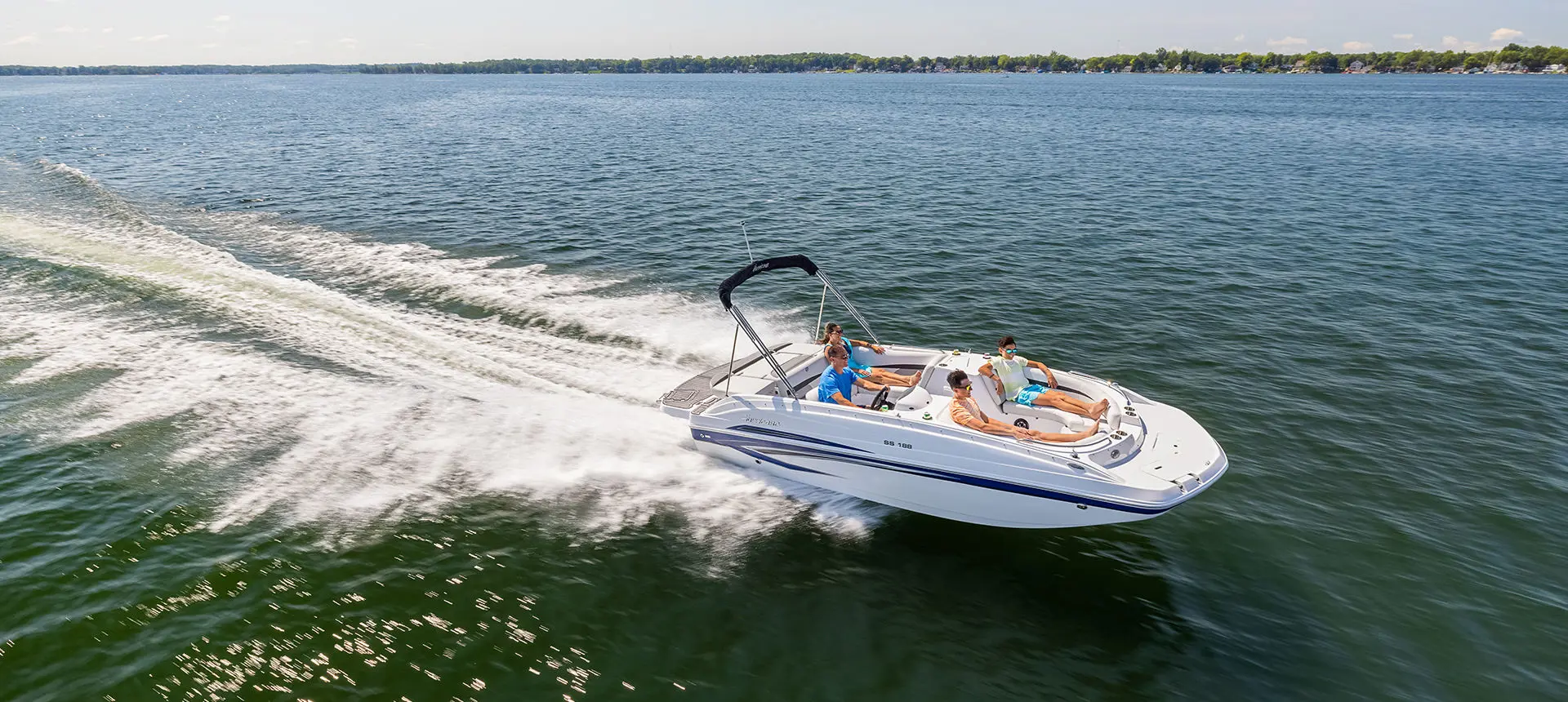 Side profile of a Hurricane SunDeck Sport 188 IO deck boat cruising on a lake.