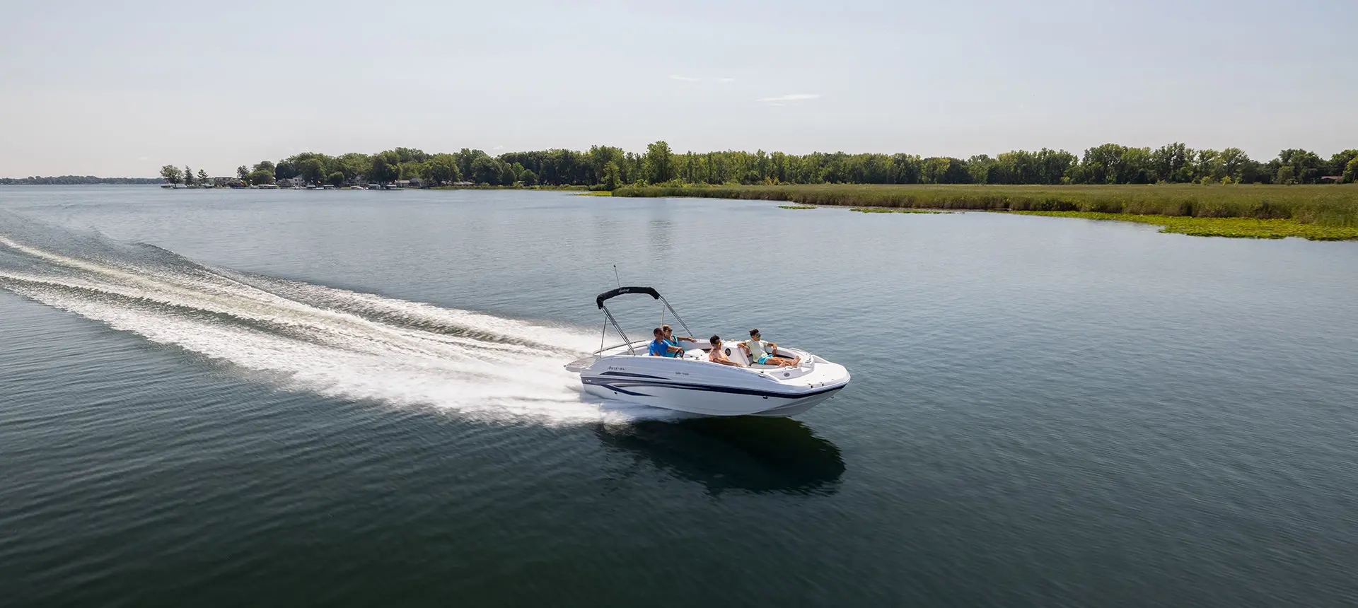 Side profile of a Hurricane SunDeck Sport 188 IO deck boat cruising on a lake.