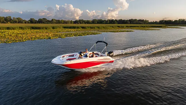 side view of a red hurricane sundeck sport ob boat cruising across a lake