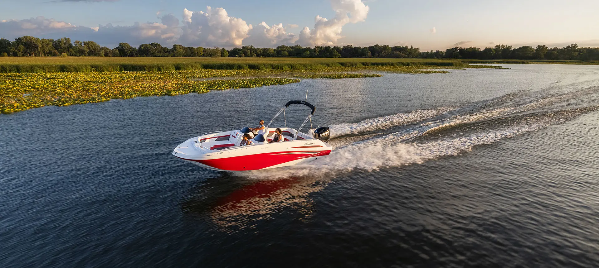 side view of a red hurricane sundeck sport ob boat cruising across a lake
