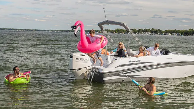 boy jumping into the water with a pink flamingo floatie off the stern of a hurricane sundeck sport ob boat