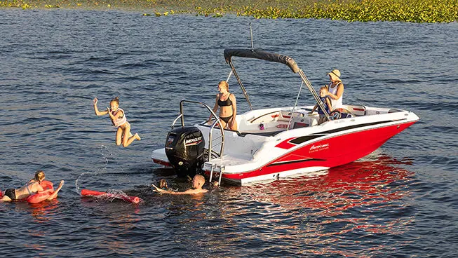 Kids and family swimming around the stern of a Hurricane SunDeck Sport OB boat.