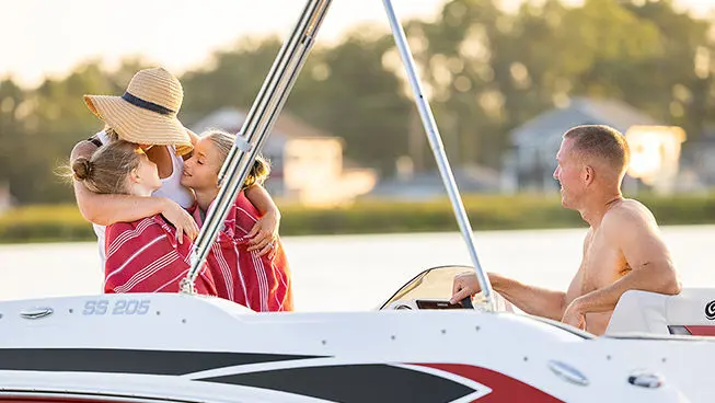 Dad watching mother and kids hugging on a Hurricane SunDeck Sport OB boat.