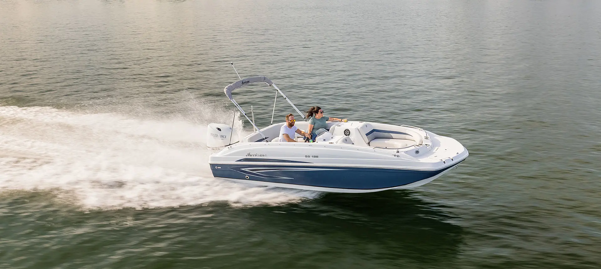 Couple speeds across a lake on a Hurricane SunDeck Sport 188 OB deck boat.