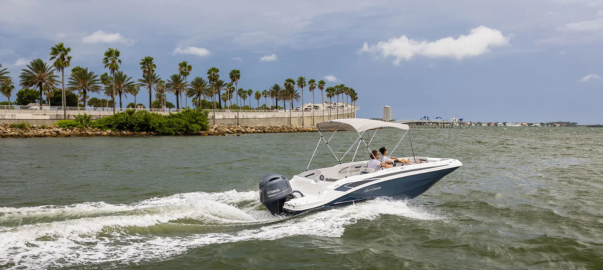 Hurricane SunDeck Sport 205 OB deck boat cruising by the coastline.