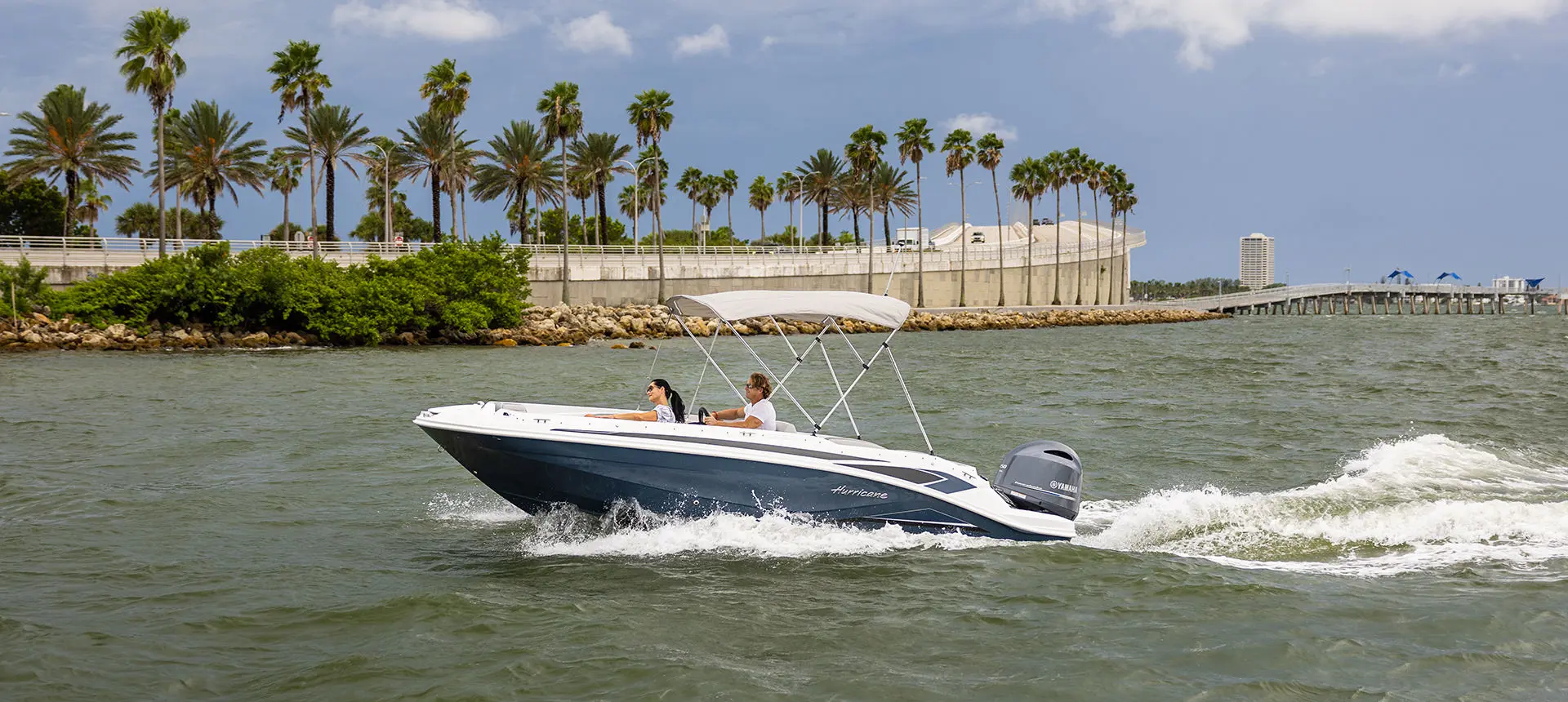 Side view of a Hurricane SunDeck Sport 205 OB deck boat near the shoreline.