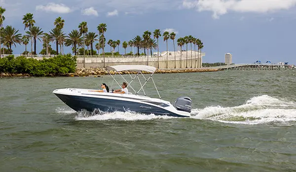 Side view of a Hurricane SunDeck Sport 205 OB deck boat near the shoreline.