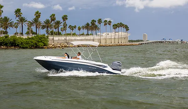 Side view of a Hurricane SunDeck Sport 205 OB deck boat near the shoreline.
