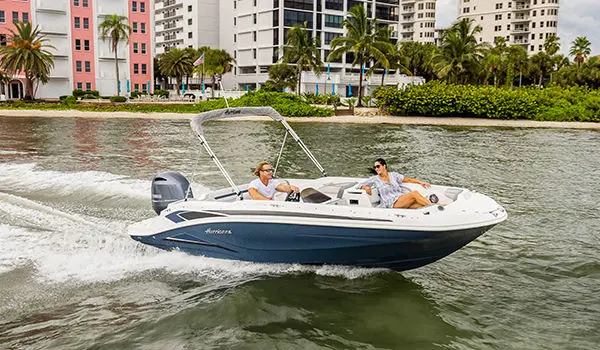 A couple cruising on a Hurricane SunDeck Sport 205 OB deck boat near the shore.