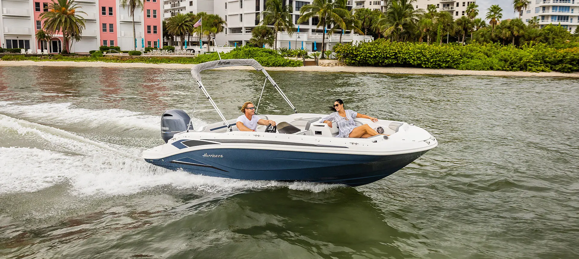 A couple cruising on a Hurricane SunDeck Sport 205 OB deck boat near the shore.