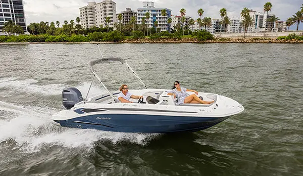 A couple smiling at each other while cruising on a Hurricane SunDeck Sport 205 OB deck boat.