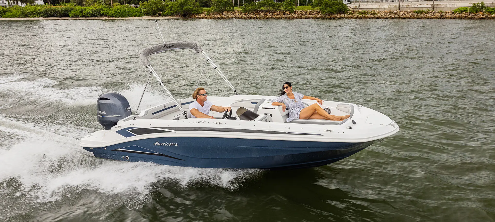 A couple smiling at each other while cruising on a Hurricane SunDeck Sport 205 OB deck boat.