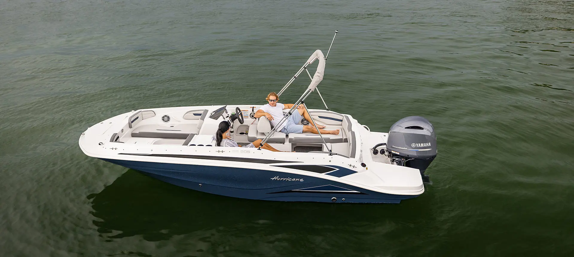 Aerial view of a couple lounging on the stern seats of a Hurricane SunDeck Sport 205 OB deck boat.