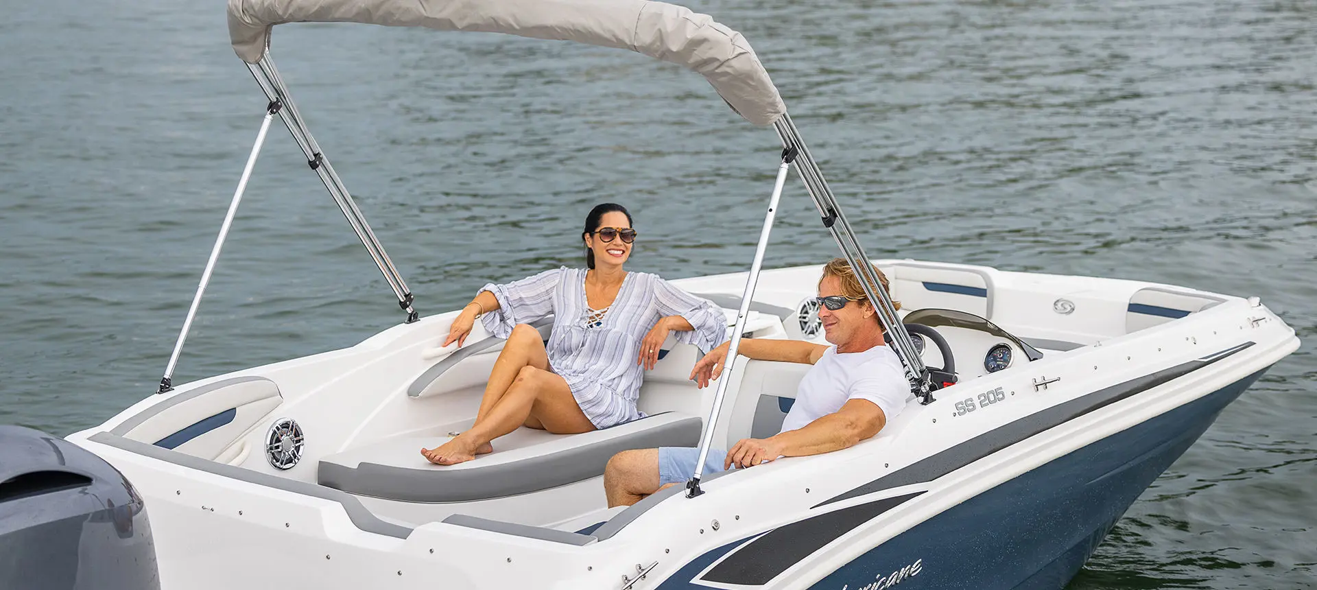 A couple smiling at each other while enjoying the stern lounge seating on a Hurricane SunDeck Sport 205 OB deck boat.