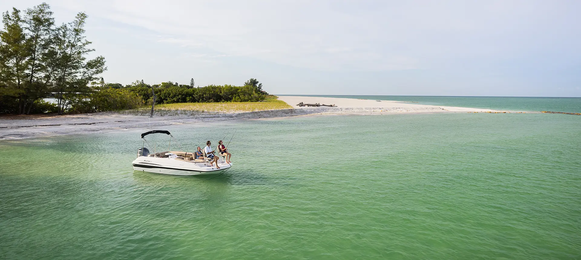 2 people fishign off the bow of a hurricane boat while near the shoreline of an ocean