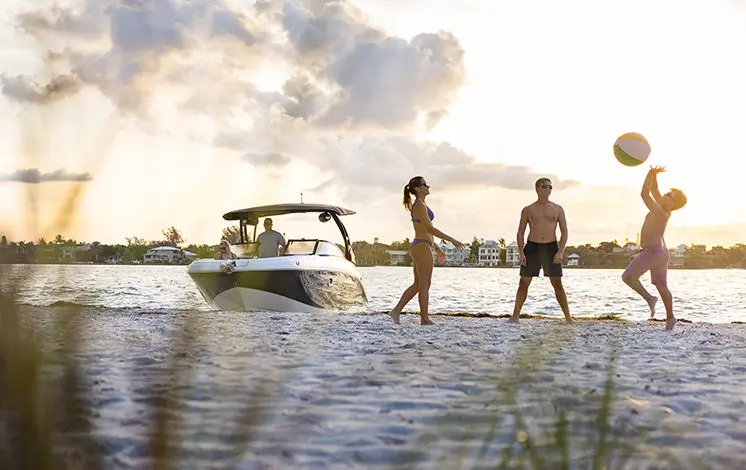 friends playing on the beach with a hurricane deck boat in the background