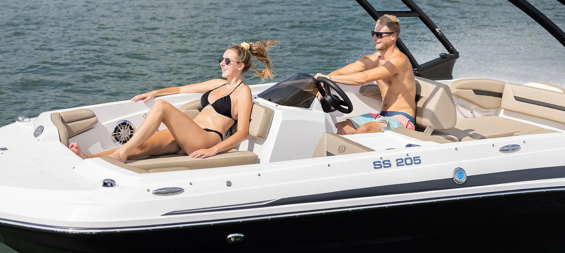 Side profile of 2 people cruising on a lake on a Hurricane SunDeck Sport 205 IO deck boat.