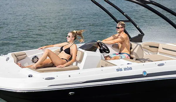 Side profile of 2 people cruising on a lake on a Hurricane SunDeck Sport 205 IO deck boat.
