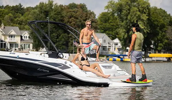 A man handing the tow rope to another man preparing to wakeboard behind a Hurricane SunDeck Sport 205 IO deck boat.