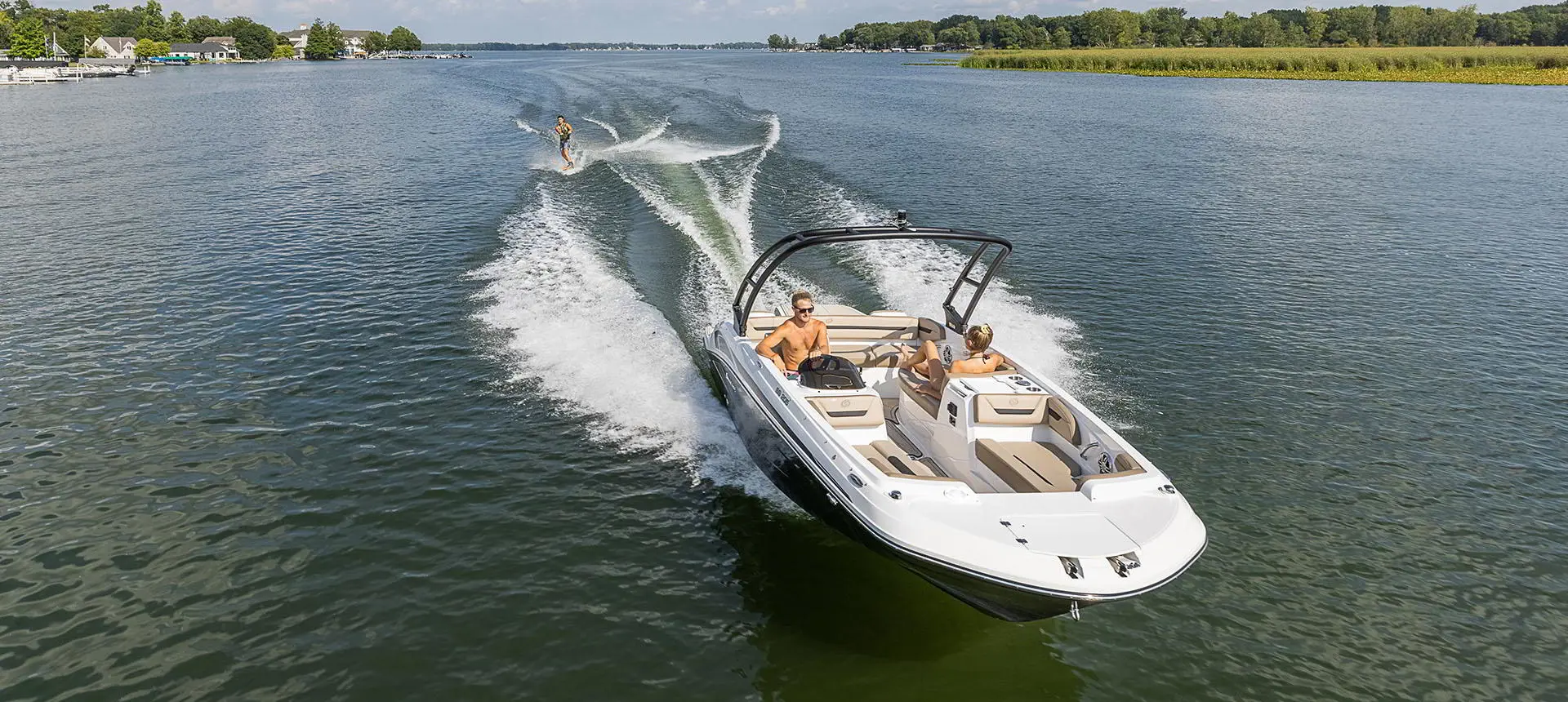 A Hurricane SunDeck Sport 205 IO deck boat pulling a wakeboarder on a lake.