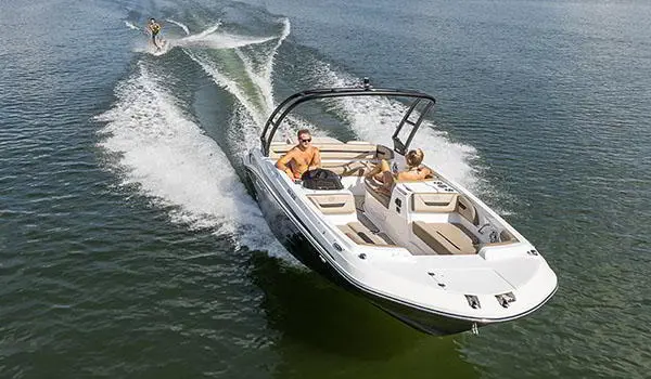 A Hurricane SunDeck Sport 205 IO deck boat pulling a wakeboarder on a lake.