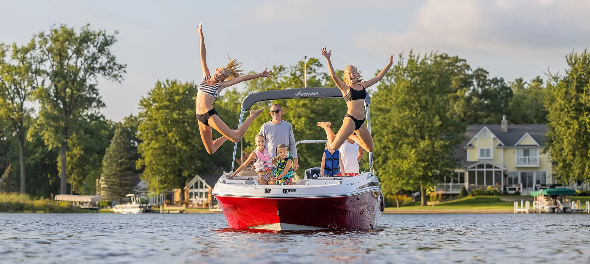 2 kids jumping into the lake off the bow of a Hurricane SunDeck Sport 205 OB deck boat.