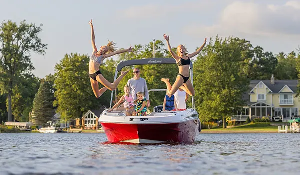 2 kids jumping into the lake off the bow of a Hurricane SunDeck Sport 205 OB deck boat.