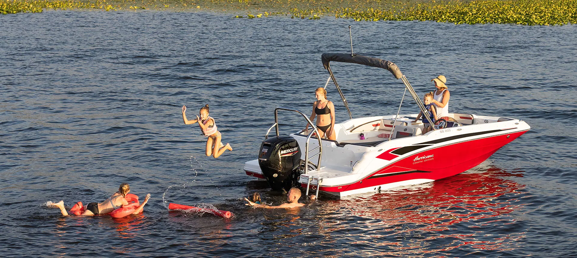 Family playing in the lake near the stern of a Hurricane SunDeck Sport 205 OB deck boat.
